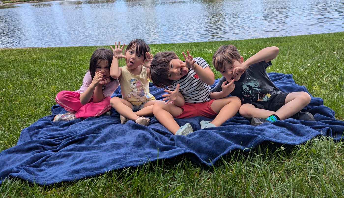 Four friends making silly faces on a picnic blanket by the pond