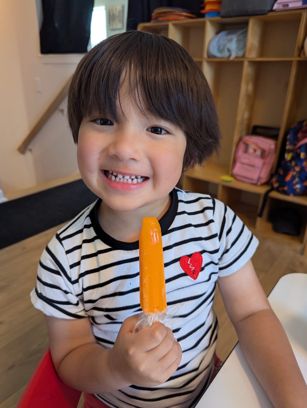 A smiling boy holding an orange popsicle