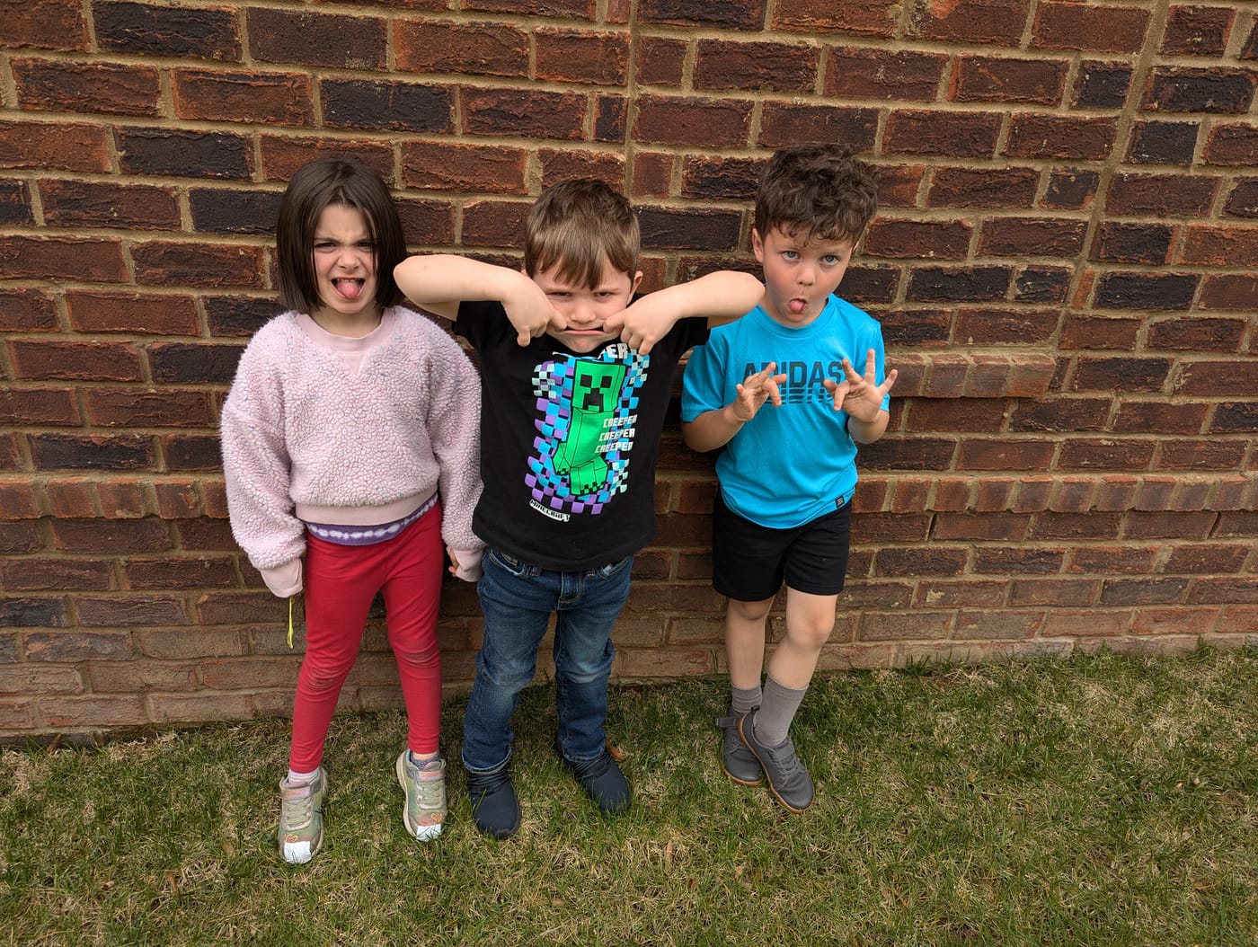 Three children making silly faces against a brick wall